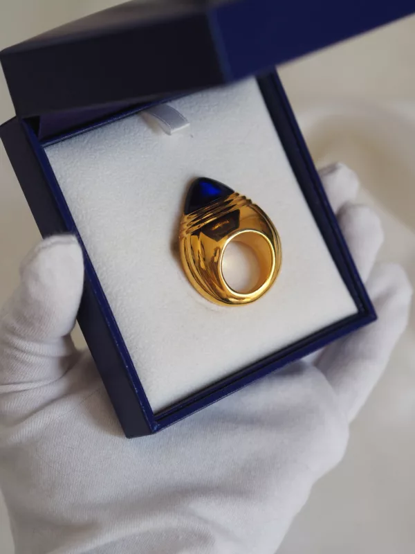 Vintage Boucheron Jaipur brooch-style perfume bottle in gold with blue cap, in original blue box, photographed on white fabric