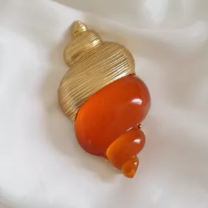 Vintage Dior Dune shell brooch in gold-tone metal and amber resin, designed by Robert Goossens, on white fabric background