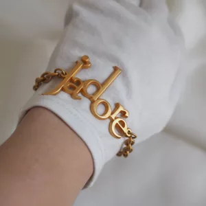 Vintage Dior J’adore bracelet with gold-tone chain and large lettering charm, photographed on ivory fabric