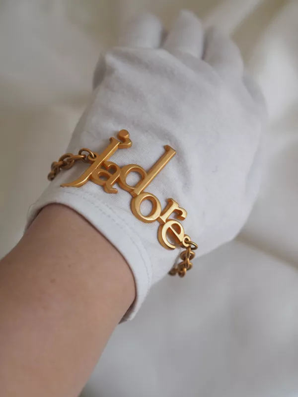 Vintage Dior J’adore bracelet with gold-tone chain and large lettering charm, photographed on ivory fabric